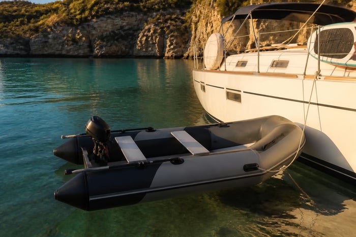 Soft inflatable catamaran tender tied alongside a moored sailing yacht in an Australian cove at golden hour