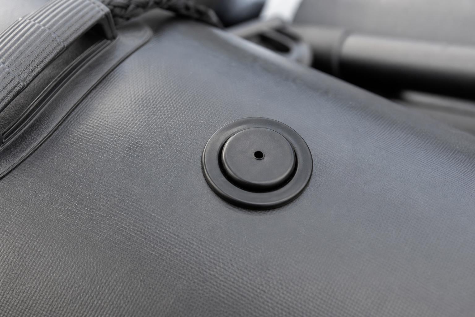 Close-up of a black plastic over-pressurisation safety valve mounted flush on a black inflatable boat tube