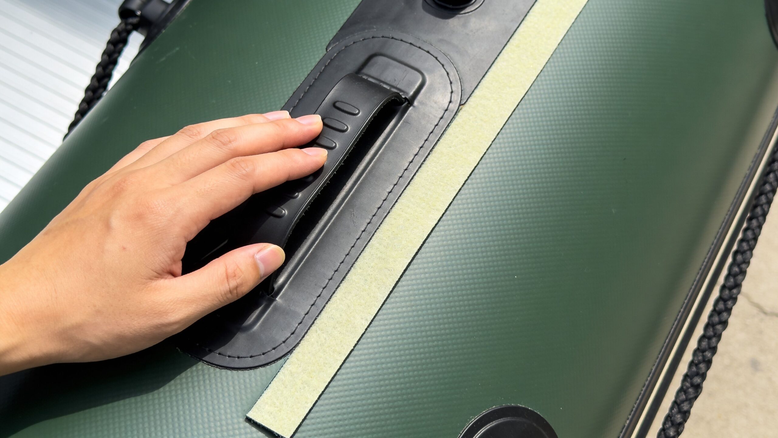 A close-up view of a person's hand touching the black handle on a green inflatable boat