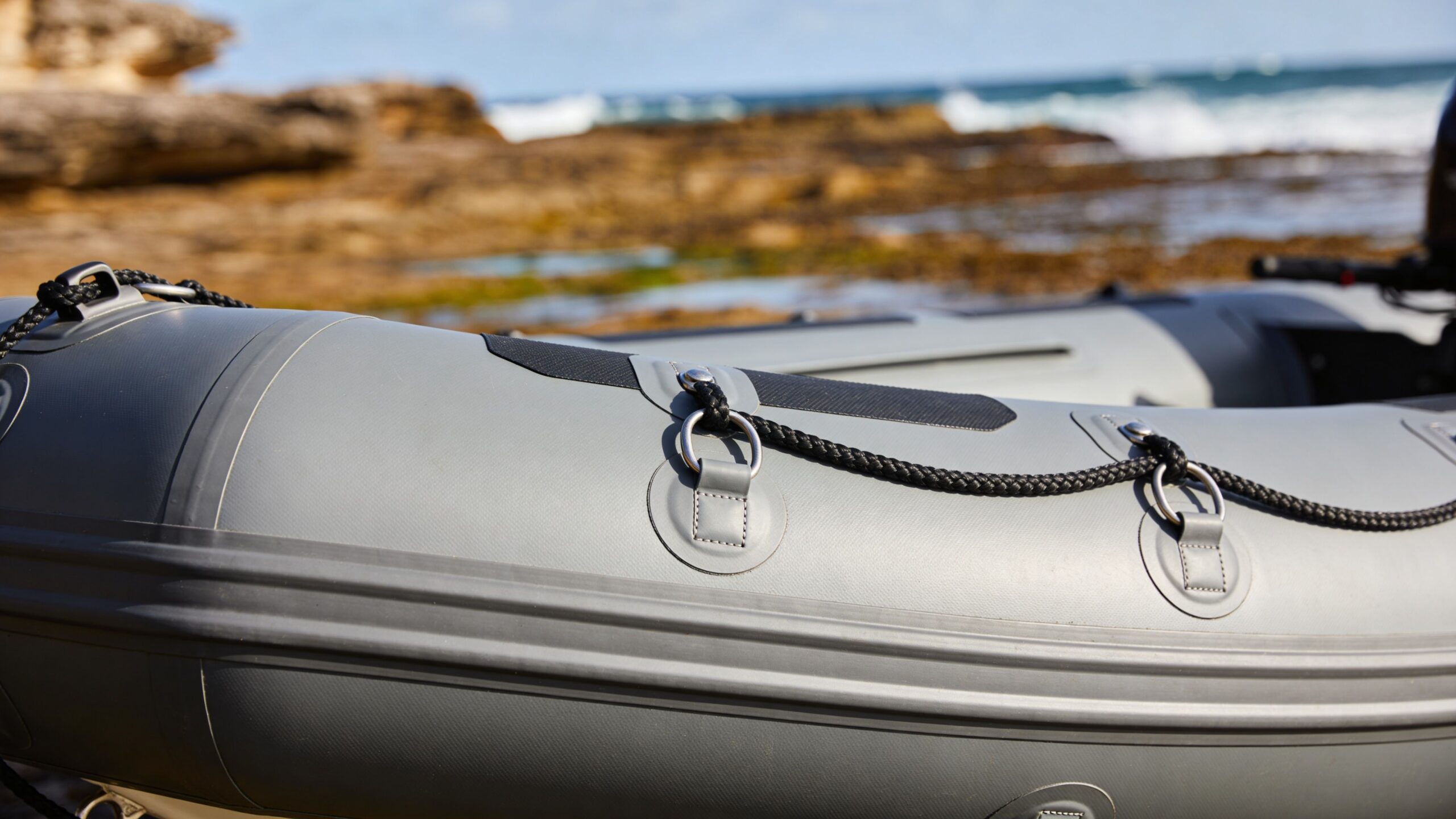 A close-up view of the side of a gray inflatable boat resting on a rocky shore.