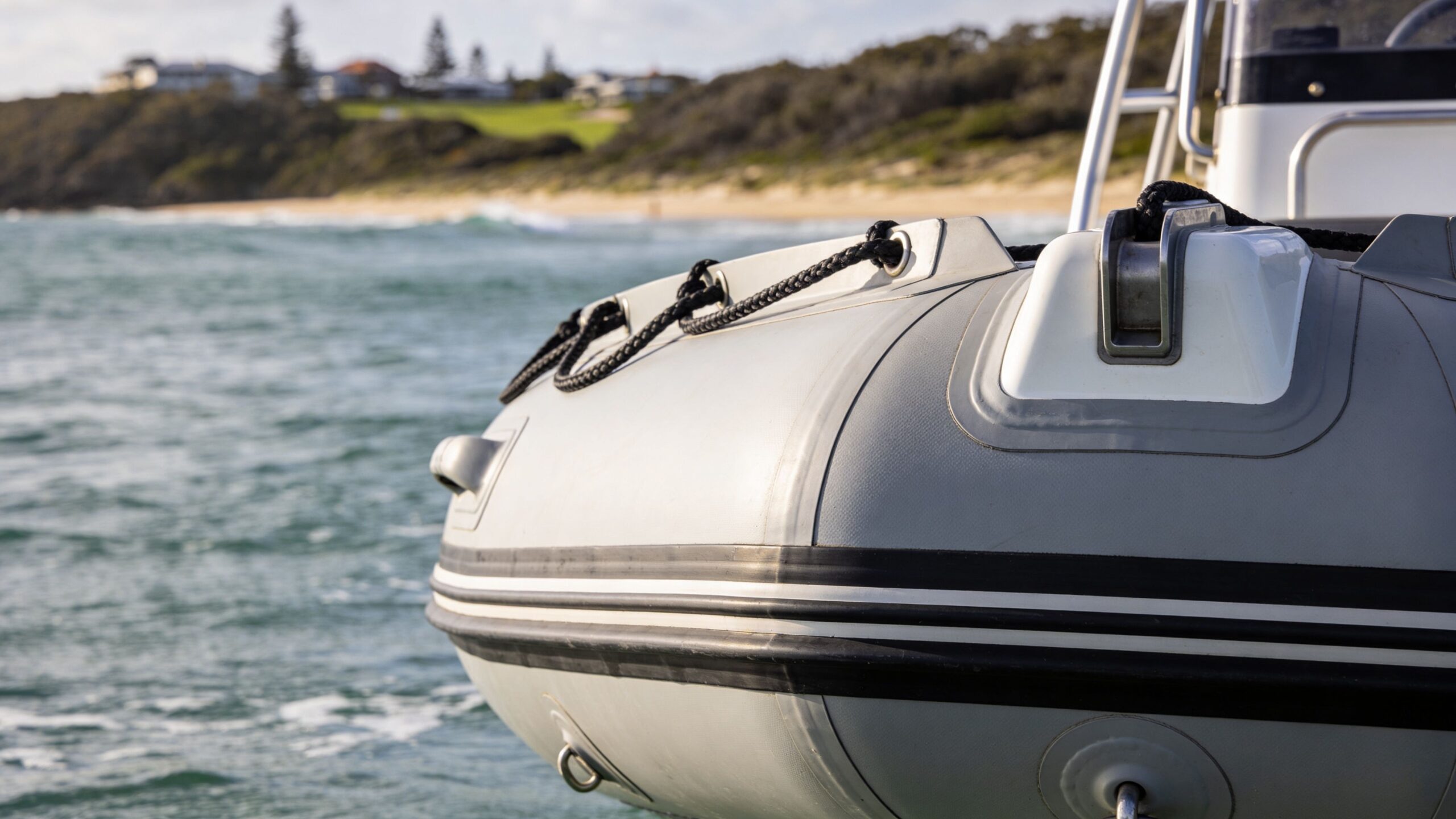 A close-up shot of the front of a grey inflatable boat floating near an Australian coastal beach.