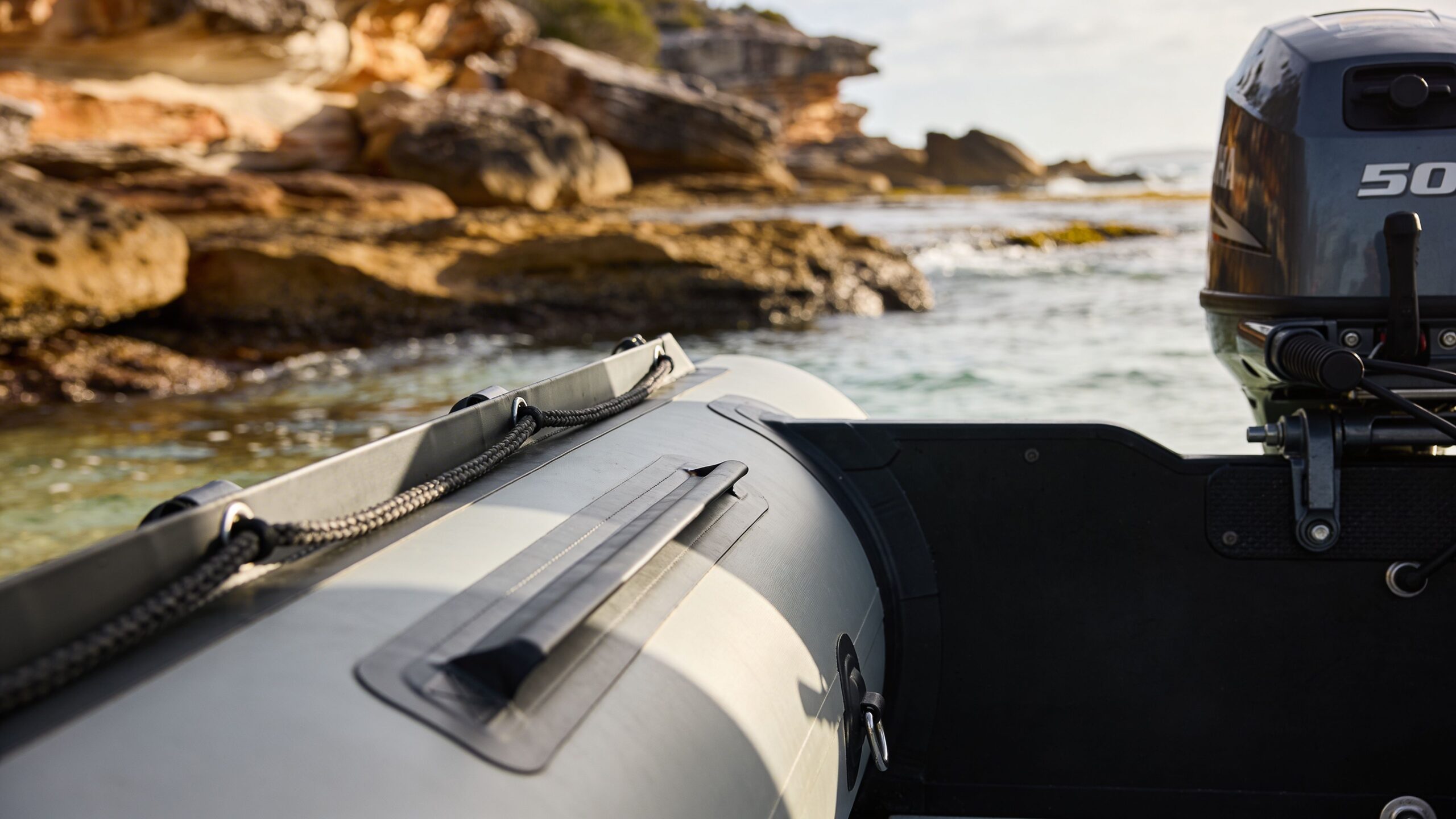 A view from inside an inflatable boat looking towards the rocky coastline with an outboard motor