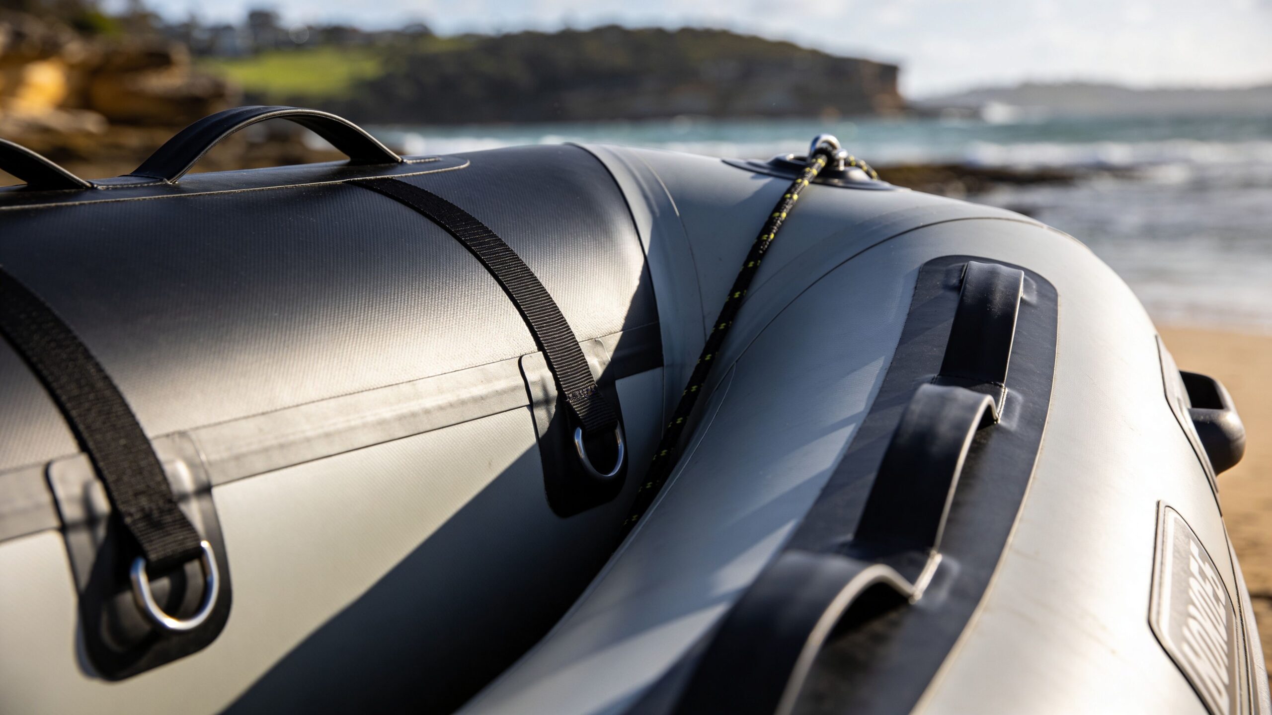 Close-up of a grey inflatable boat on a sandy beach near the ocean shoreline.