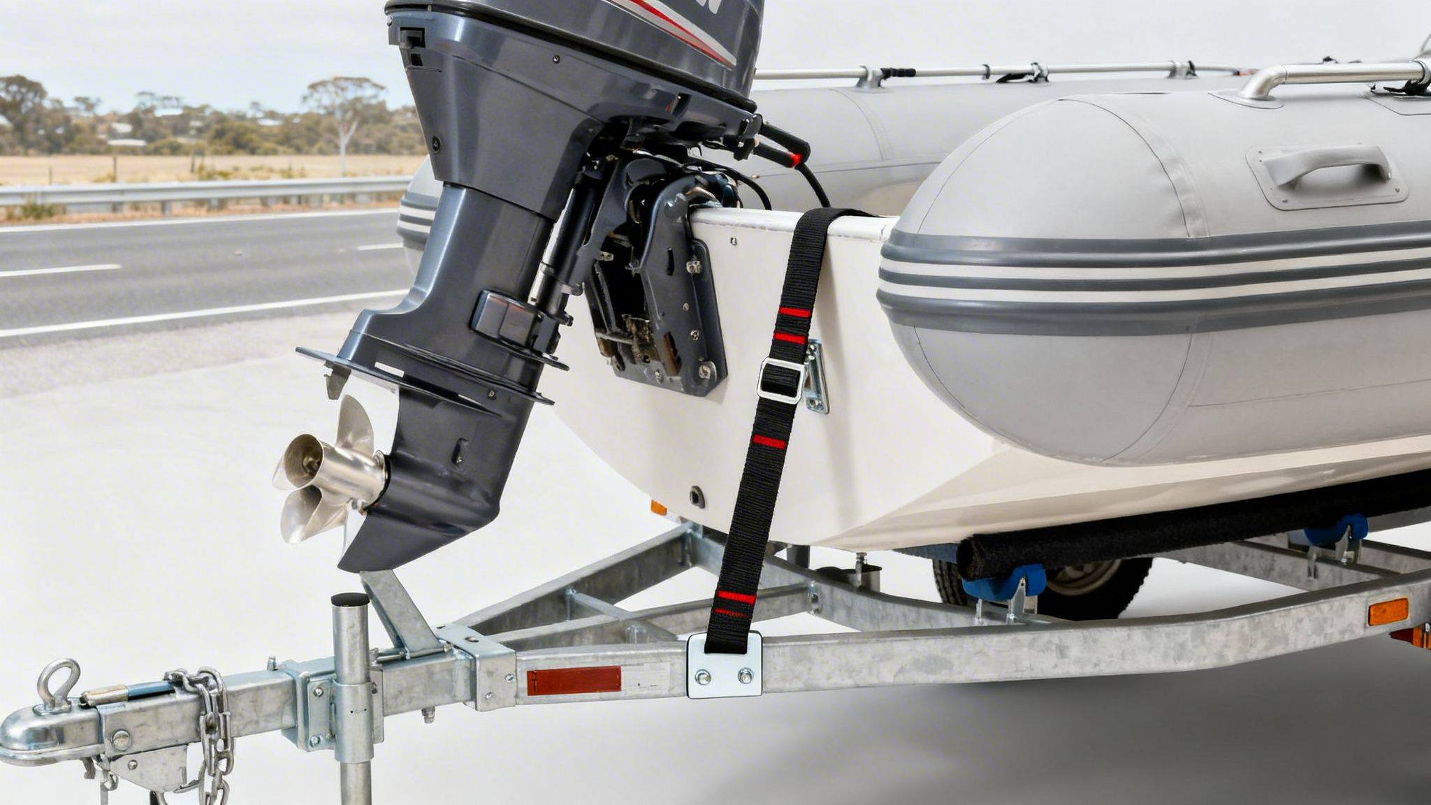 Close-up of an inflatable boat with an outboard motor securely tied down on a galvanized trailer.