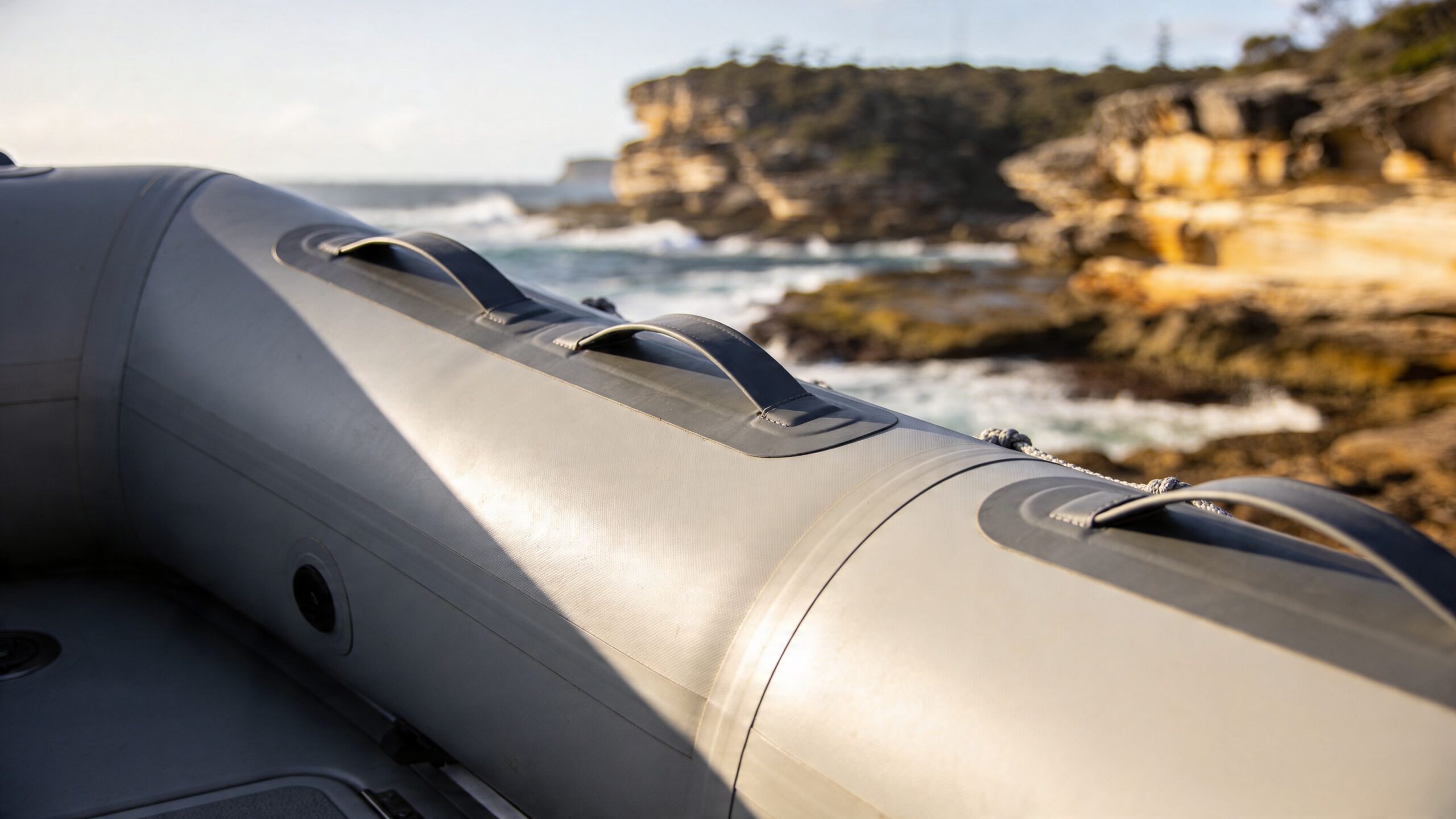 A close-up view of a grey inflatable boat with safety handles, floating near a rocky coastline in Australia.