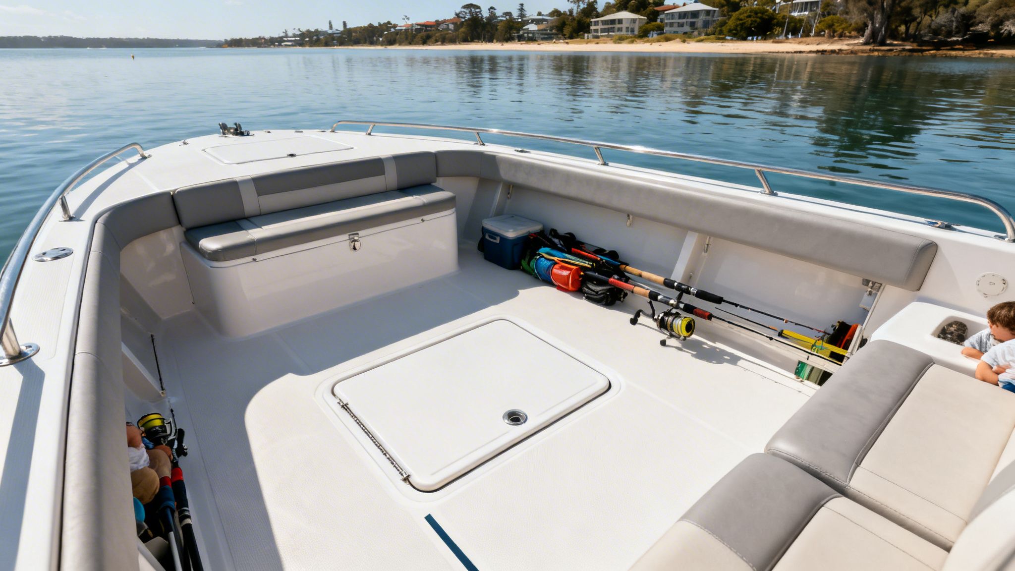 A clean white boat deck with fishing rods, a cooler, and an underfloor hatch.