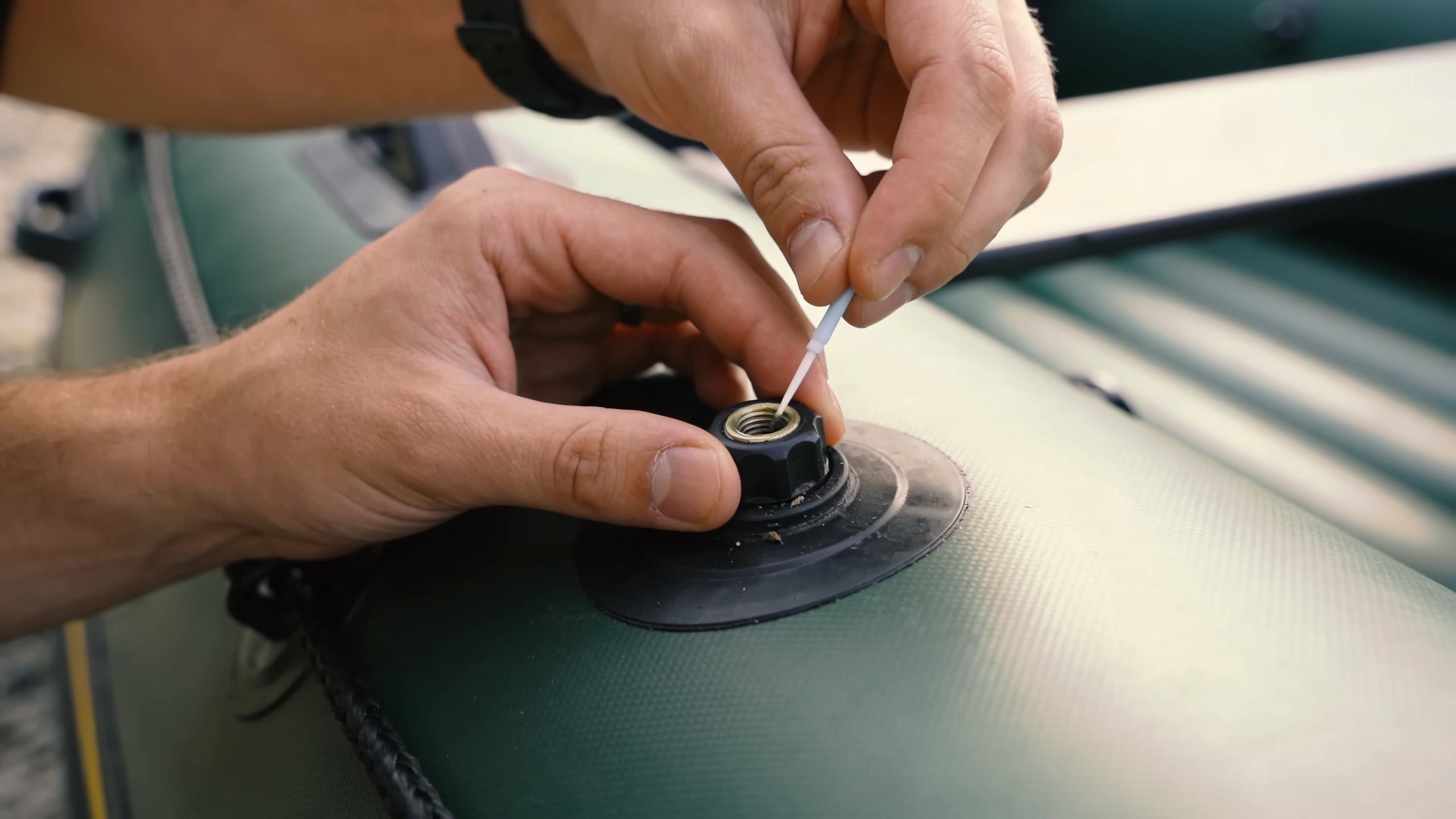 A person carefully applying lubricant or sealant to an inflatable dinghy valve using a small brush.