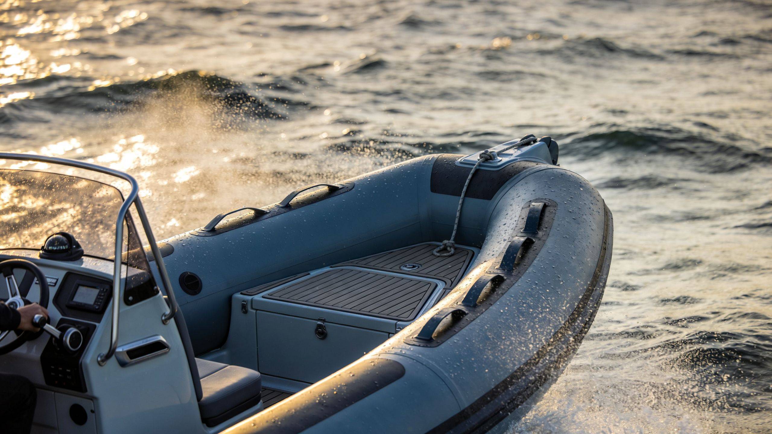A close-up view of a grey rigid inflatable boat traveling across choppy water at sunset.
